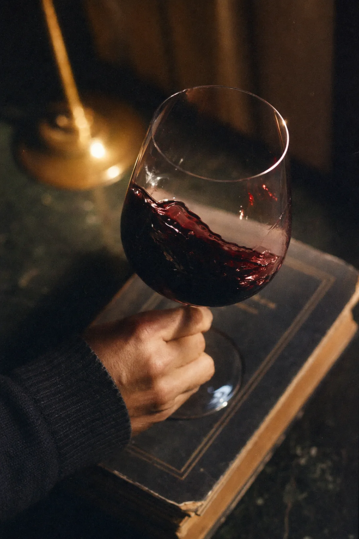A single crystal glass of cabernet being swirled over an old book