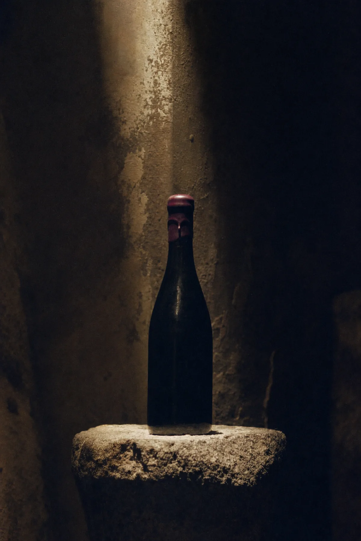An unlabelled dark bottle with a plum wax seal on a stone plinth in the cellar